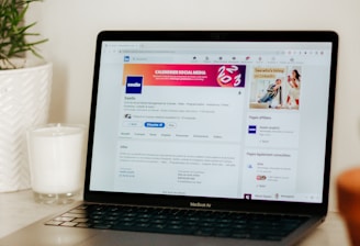 A laptop displaying a LinkedIn profile page is placed on a light-colored surface. To the left of the laptop, there is a white candle in a glass holder and a green plant in a white textured pot.